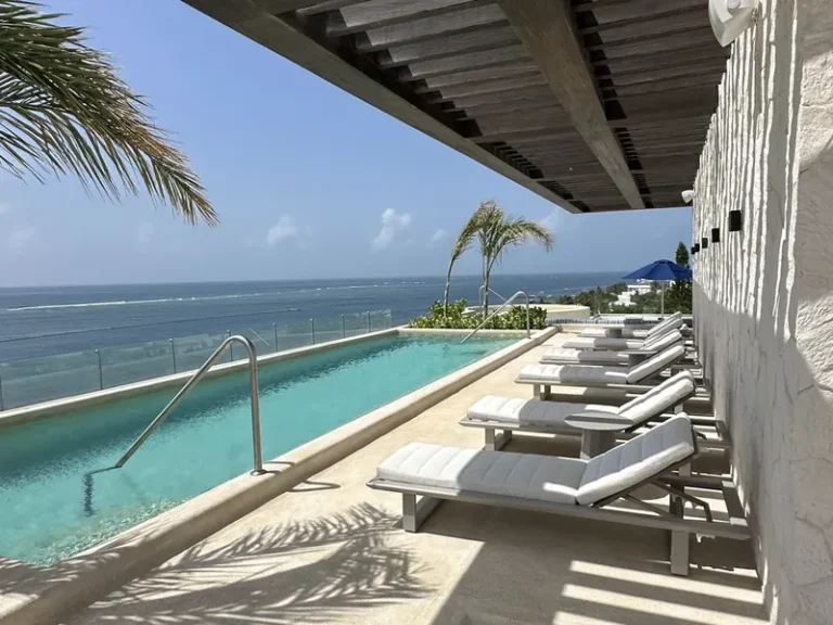 Alberca de Sole BLU con camastros alineados bajo una pérgola de madera y vista al mar Caribe